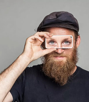 Foto de divulgação do app Be My Eyes. Homem segura smartphone em frente aos seus olhos. Na tela do aparelho, no lugar em que deveriam estar os olhos do homem, aparecem os olhos de outra pessoa.