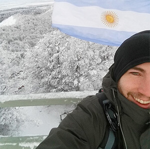 Pepe em frente à bandeira da Argentina. Atrás, muitas árvores cobertas de neve.