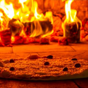 pizza redonda com massa fina em frente ao fogo do fogão a lenha