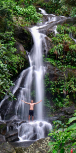 Foto de uma grande cachoeira e um homem de braços abertos virado para a cachoeira.