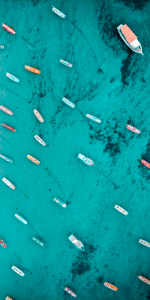 Foto aérea do mar com águas cristalinas com muitos barquinhos no mesmo.