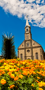 Foto de uma igreja ao fundo e algumas flores em tons de laranja e amarelas em primeiro plano.