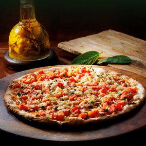 pizza redonda em cimade uma tábua, em uma mesa de madeira, com azeite aromatizado ao fundo