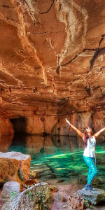 Foto de uma menina de braços abertos dentro de uma caverna com um lago dentro do mesmo.