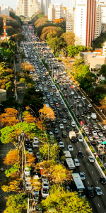 Foto aérea de uma rua cheia de carros com algumas árvores e prédios no entorno.