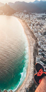 Foto aérea da praia com areia, ondas e a cidade do lado direito.