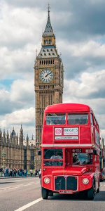 Foto em primeiro plano de um ônibus clássico de Londres e ao fundo o monumento do relógio Bigben.