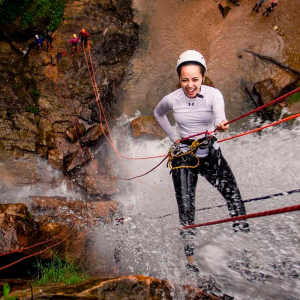 Mulher sorrindo e descendo de rapel uma cachoeira.