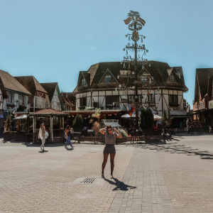 Menina posando para a foto com algumas casas de comércio ao fundo em um dia ensolarado