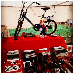 Foto da bancada de um kiosque da feira com máquinas de escrever e uma bicicleta infantil á venda.