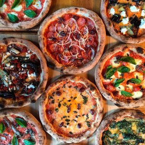 várias pizzas redondas enchendo completamente a foto, de diversos sabores