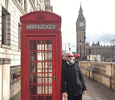 Lucas encostado em tradicional cabine telefônica vermelha, na cidade de Londres. Big Ben ao fundo.