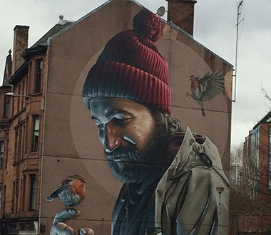 Urban Art: pintura realizada na parede de sobrados em Glasgow, Reino Unido. Homem com touca cercado por passarinhos.