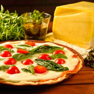 pizza marguerita redonda com massa bem fininha, em cima de uma tábua, com queijo, azeite e alecrim atrás