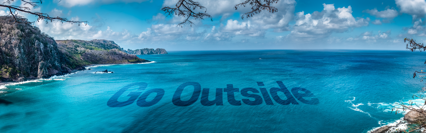 Foto panorâmica de praia em Fernando de Noronha, mar azul e calmo com arquipélagos ao fundo. Letreiro Go Outside aparece sobre a água.
