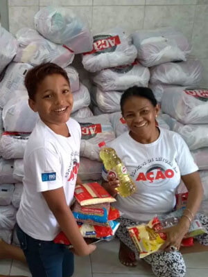 Um menino e sua mãe tem frente a sacolas do Natal sem Fome segurando alimentos e sorrindo