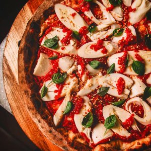 pizza redonda em cima de uma tábua com bastante palmito e molho de tomate e folhas verdes