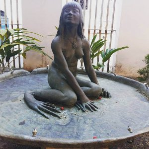 Escultura de híbrido mulher-rã sentada sobre vitória-régia.